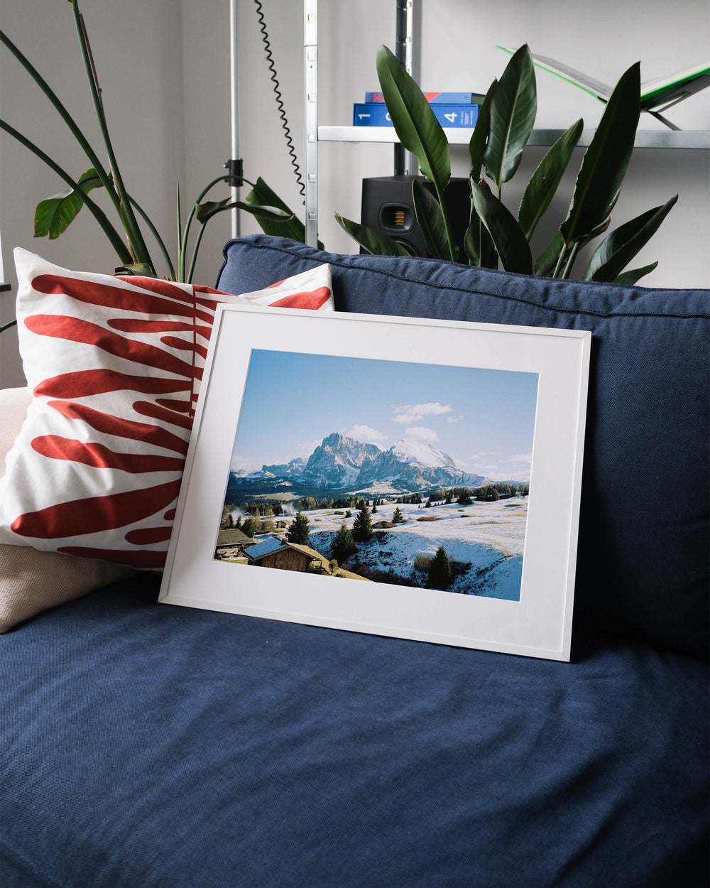 Framed analog photo print on Fujifilm paper featuring Sasso Lungo in the Dolomites on a clear winter day. With snow-covered peaks glowing under the sun and blue skies above, displayed on a blue couch with a minimalist interior setting.