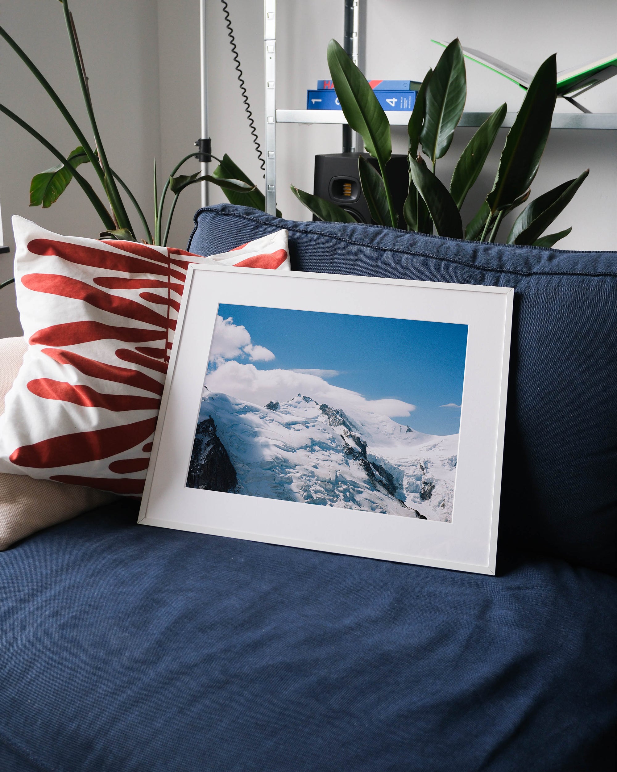 Framed analog photo print on Fujifilm paper featuringMont Blanc, partially hidden by mist and swirling clouds, captured from the Aiguille du Midi at 3842 meters. Displayed on a blue couch with a minimalist interior setting.