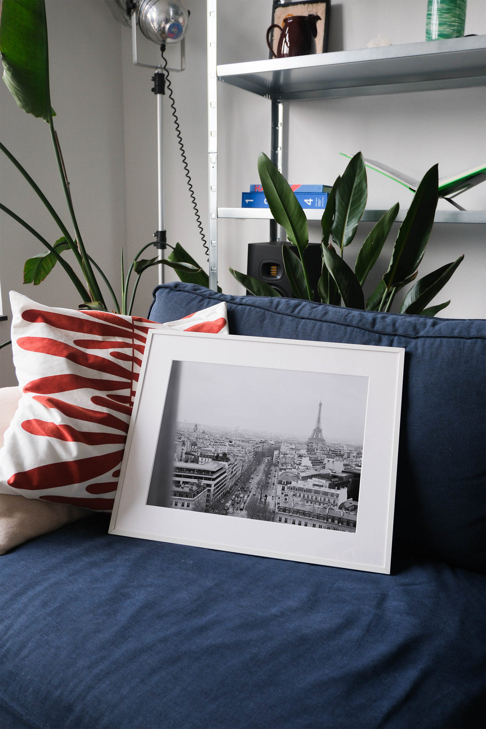 Framed analog photo print on Fujifilm paper featuring the Eiffel Tower as seen from the Arc de Triomphe in Paris on a winter day, captured in black and white film for a classic, timeless look. Displayed on a blue couch with a minimalist interior setting.