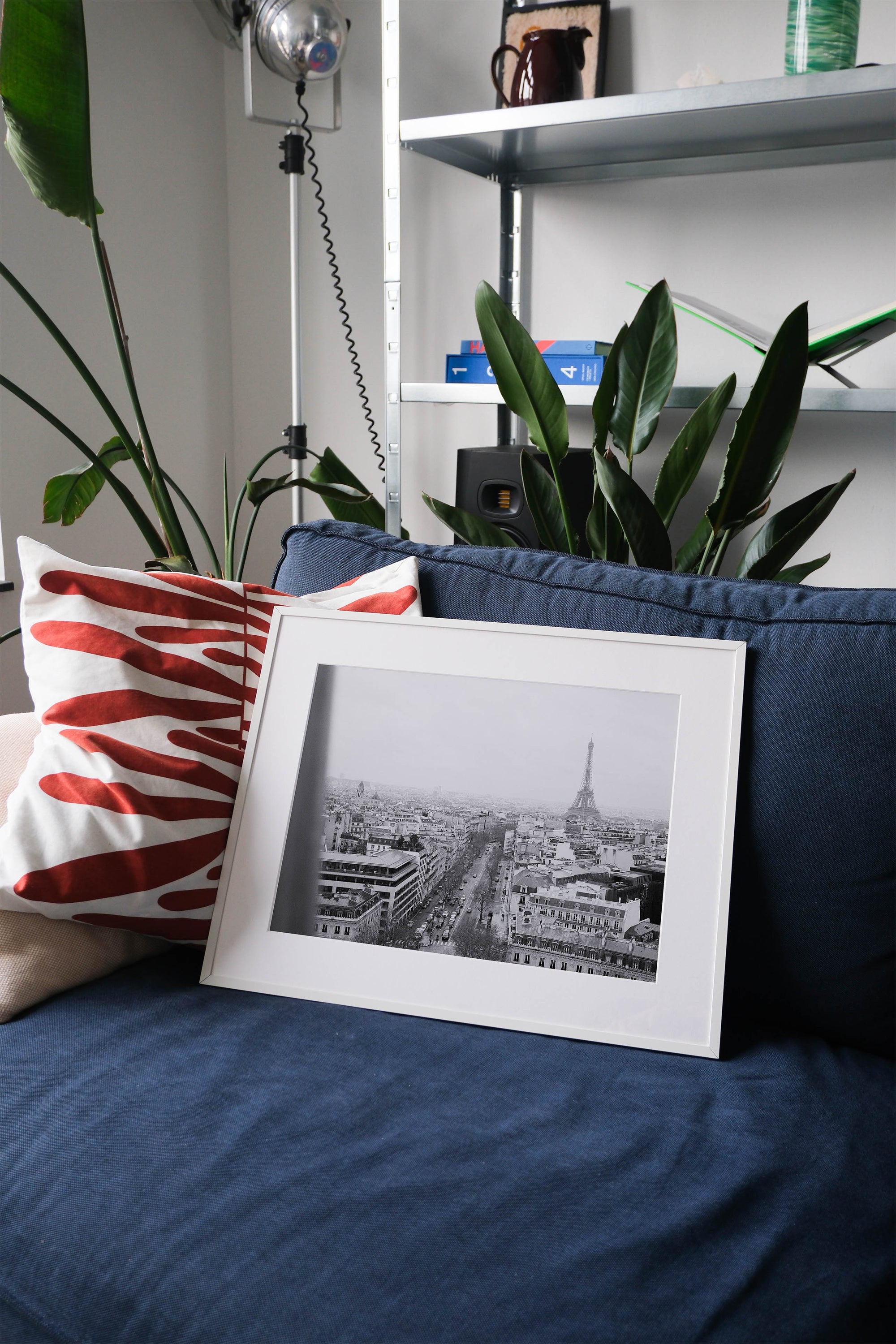 Framed analog photo print on Fujifilm paper featuring the Eiffel Tower as seen from the Arc de Triomphe in Paris on a winter day, captured in black and white film for a classic, timeless look. Displayed on a blue couch with a minimalist interior setting.