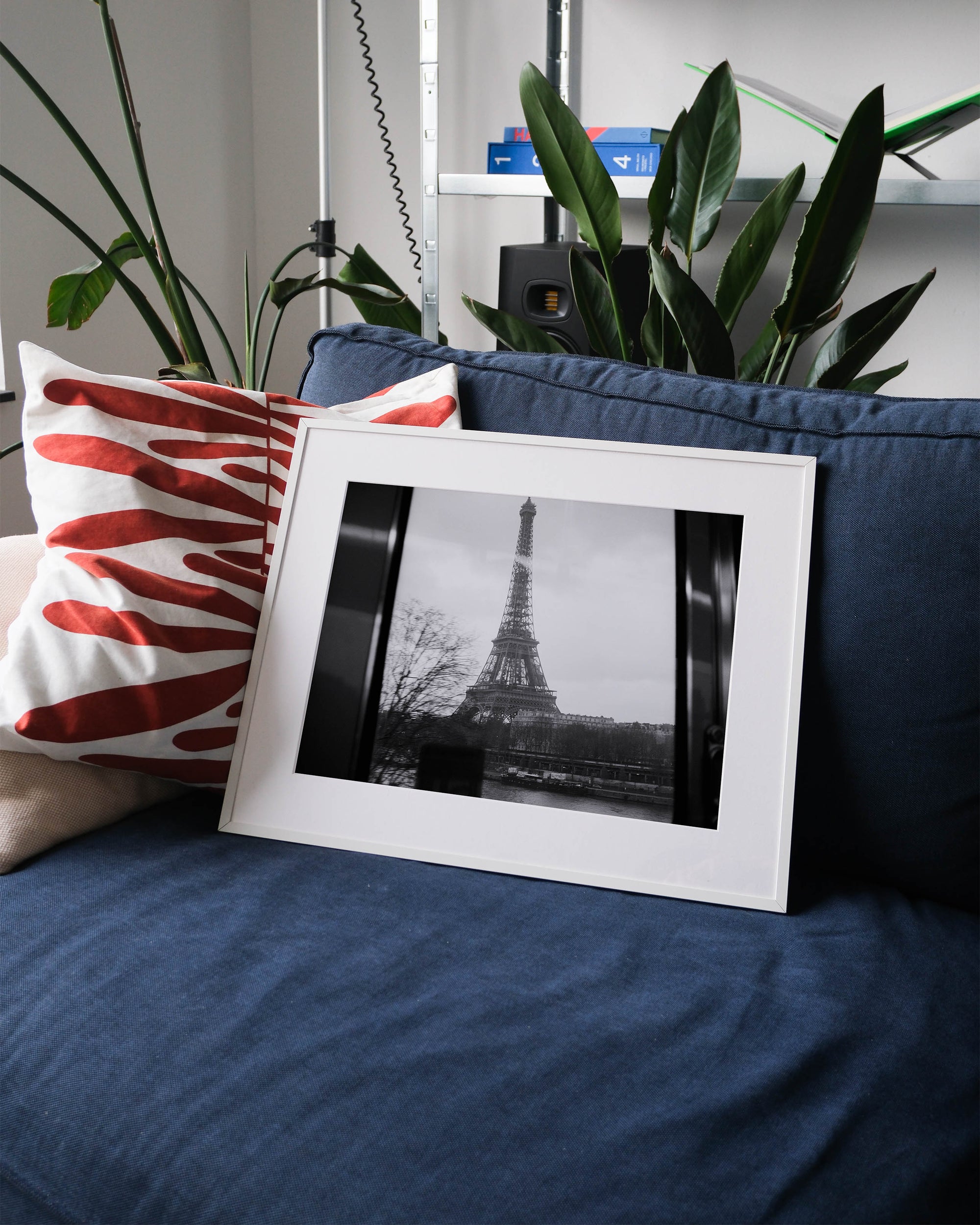 Framed analog photo print on Fujifilm paper featuring the Eiffel Tower as seen from Metro Line 6 above the Seine, captured in black and white film, displayed on a blue couch with a minimalist interior setting.