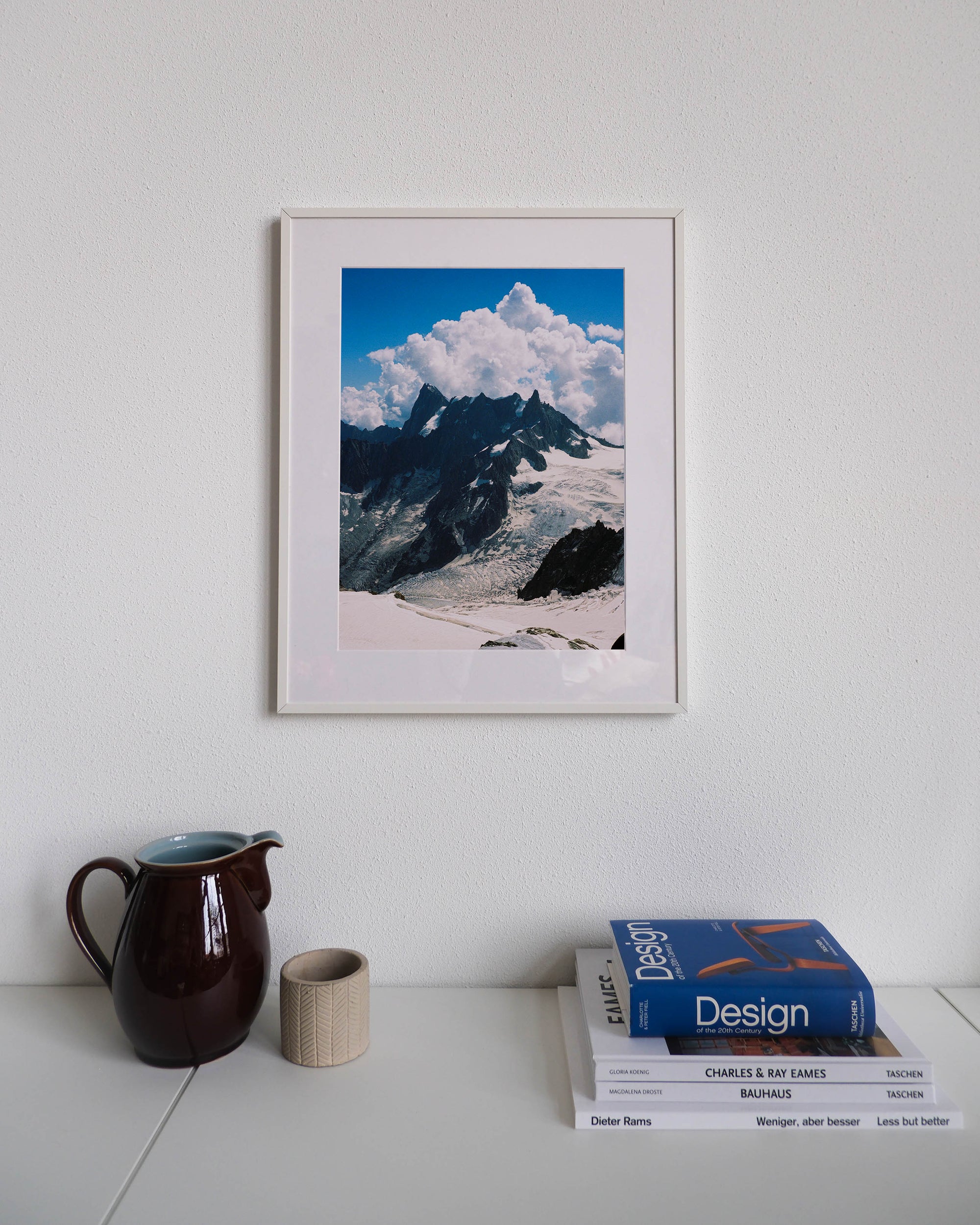 Framed analog photo print on Fujifilm paper featuring the towering peaks of the Mont Blanc massif, showcasing the rugged, snow-capped summits against the sky, displayed on a modern white cabinet with a minimalist interior setting.