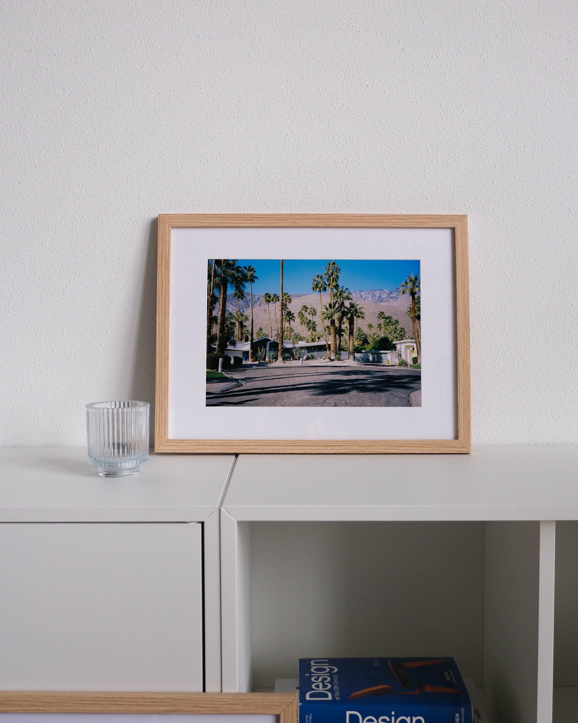Framed analog photo print on Fujifilm paper featuring a road with midcentury modern homes in Palm Springs, displayed on a modern white cabinet with a minimalist interior setting.