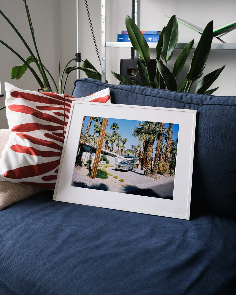 Framed analog photo print on Fujifilm paper featuring a midcentury modern home in Palm Springs, with tall palm trees under a sunny sky and a vintage Ford Ranchero parked in front, displayed on a blue couch with a minimalist interior setting.