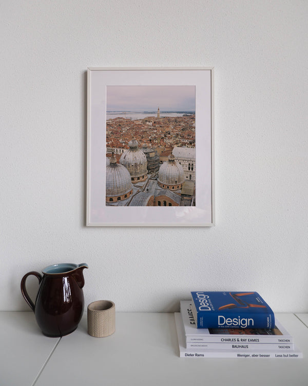 Framed analog photo print on Fujifilm paper featuring the Basilica di San Marco rising above Venice’s terracotta rooftops, captured from the Loggetta del Sansovino. Displayed on a modern white cabinet with a minimalist interior setting.
