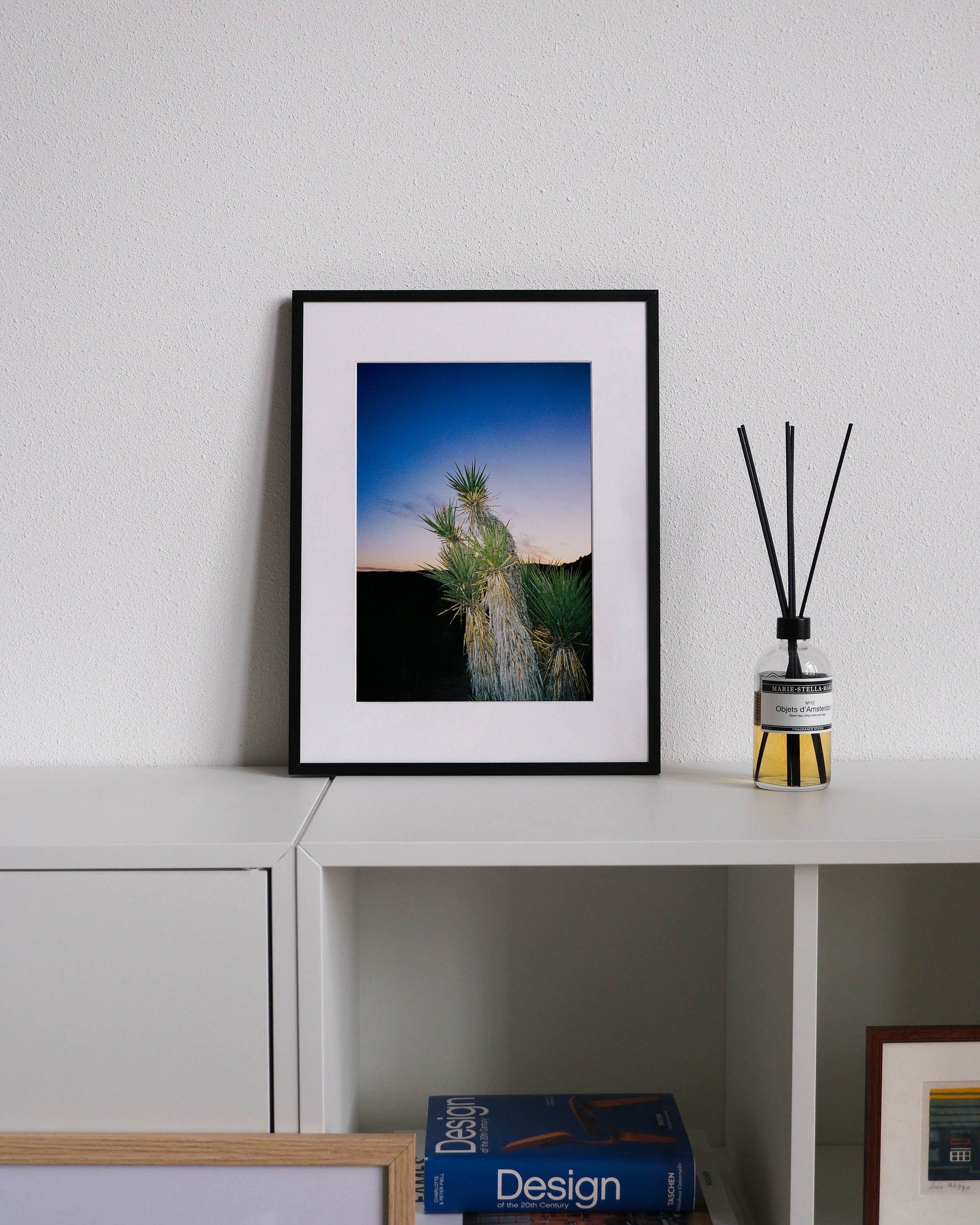 Framed analog photo print on Fujifilm paper featuring Yucca brevifolias in Joshua Tree at sunset, with the sky fading into twilight and the landscape transitioning to dusk, displayed on a modern white cabinet with a minimalist interior setting.