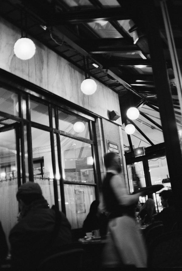 Black-and-white analog photo print featuring the iconic Café du Flore in Saint-Germain-des-Prés, with a busy waiter serving guests amidst the café's classic Parisian ambiance.