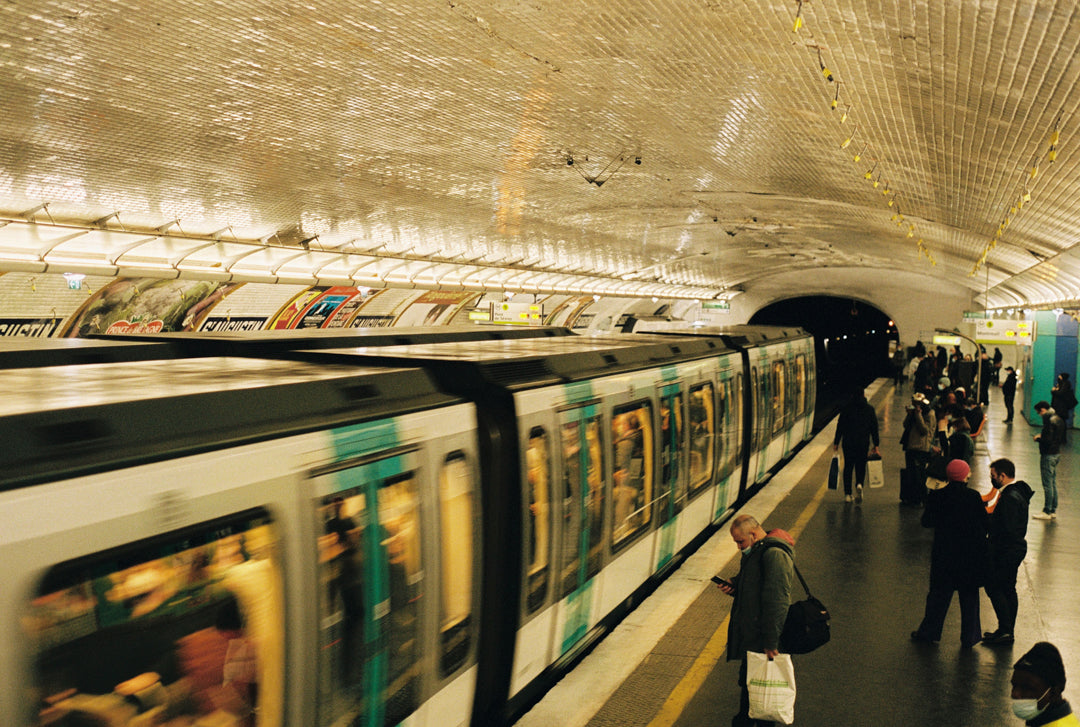 Analog photo print on film featuring a scene inside the Paris metro, with a man checking his phone while waiting for the subway, capturing the fast-paced rhythm of city life.