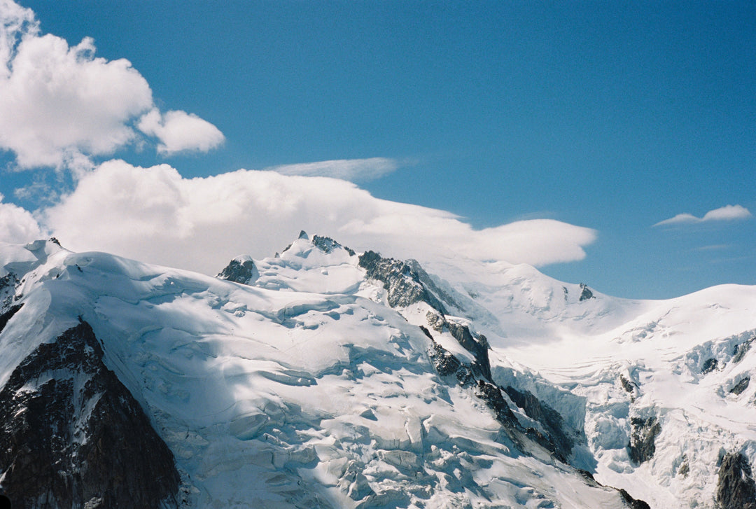 Analog photo print on Fujifilm paper featuring Mont Blanc, partially hidden by mist and swirling clouds, captured from the Aiguille du Midi at 3842 meters. The towering peaks fade into the mist, adding an air of mystery to the majestic landscape.