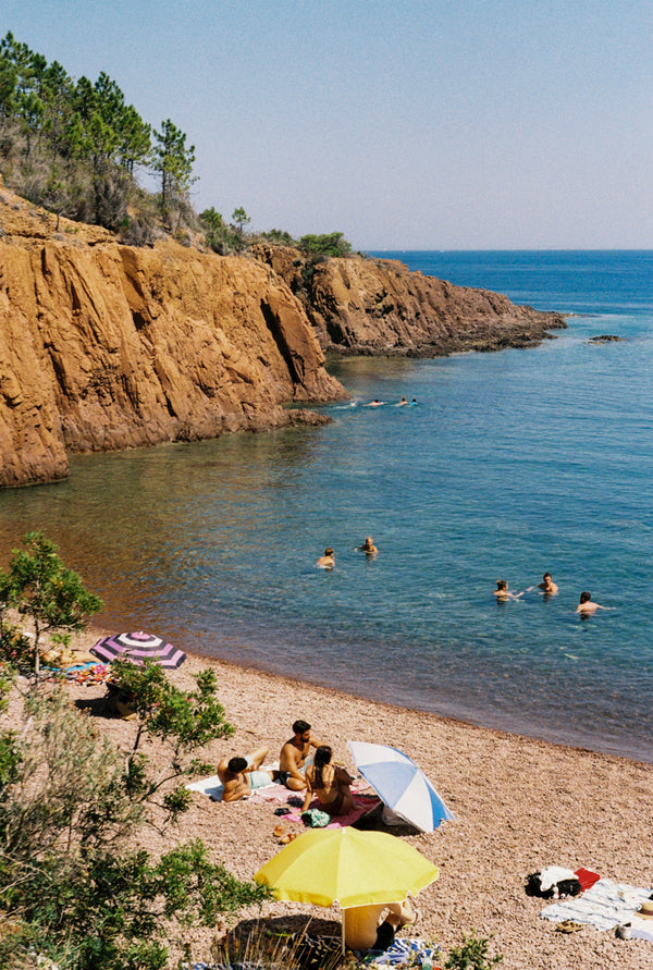 Analog photo print featuring the vibrant atmosphere of Cap Roux, with parasols shading sunbathers on warm stones and others cooling off in the Mediterranean, set against the striking contrast of red rocks and the blue sea.