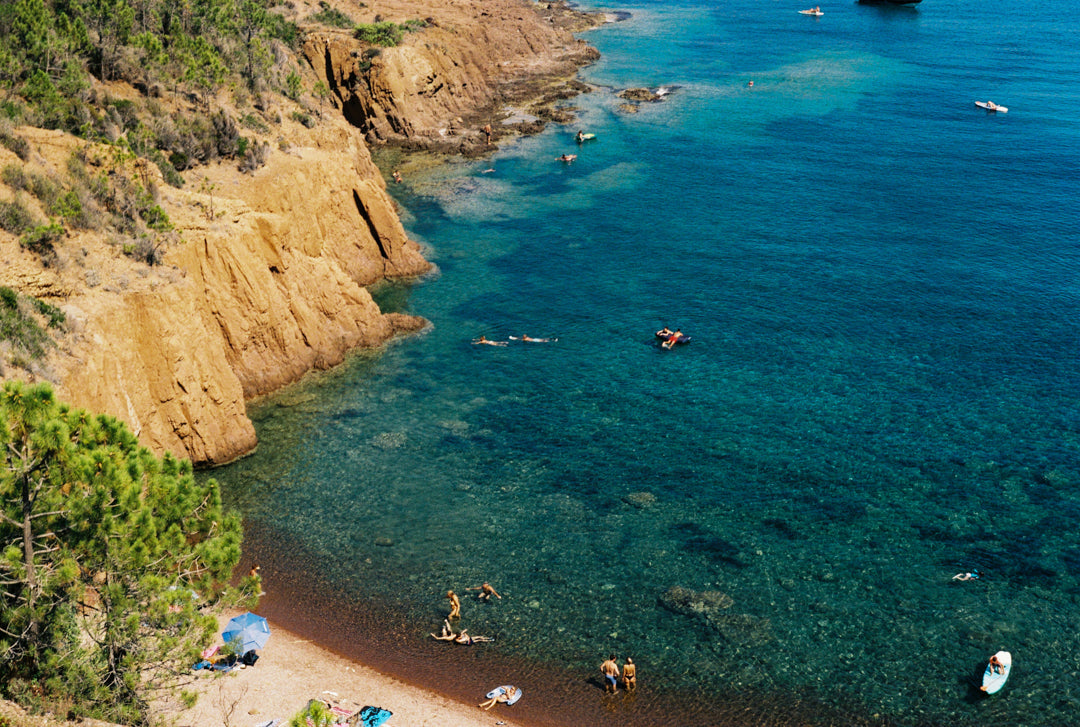 Analog photo print featuring the vibrant contrast of the blue Mediterranean waters and red rocks of Cap Roux, with people enjoying the clear sea on the Côte d'Azur.